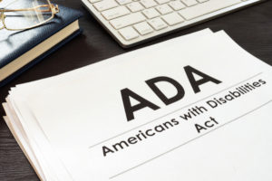 a stack of papers with the title ADA Americans with Disabilities Act next to a computer keyboard